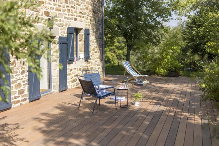 WPC-Terrasse Silvadec Atmosphere in Ipé-Optik an einem Natursteinhaus mit Gartenmöbeln